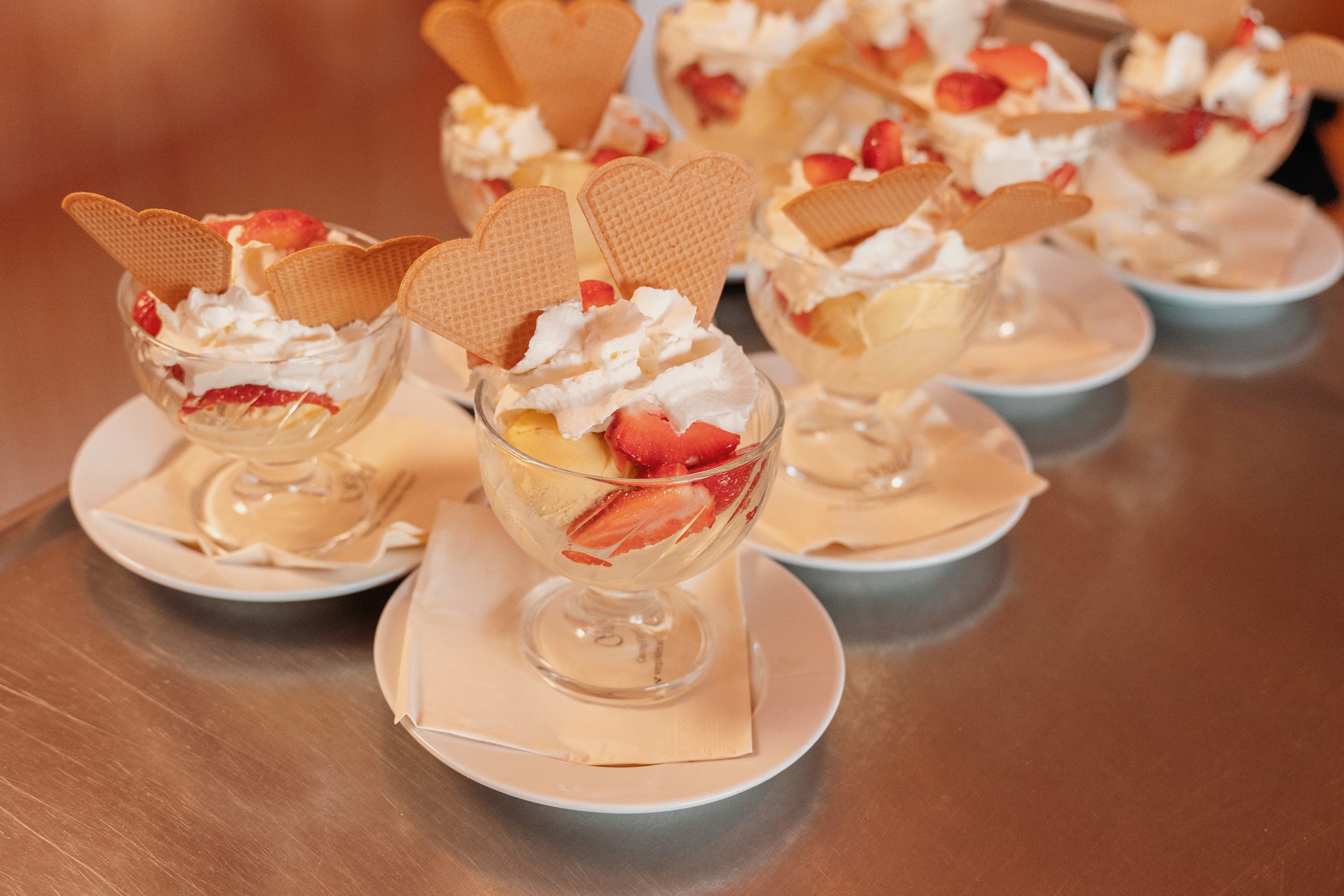Reihe Eisbecher mit Erdbeeren, Sahne und Waffelherzen, bereit zum Servieren