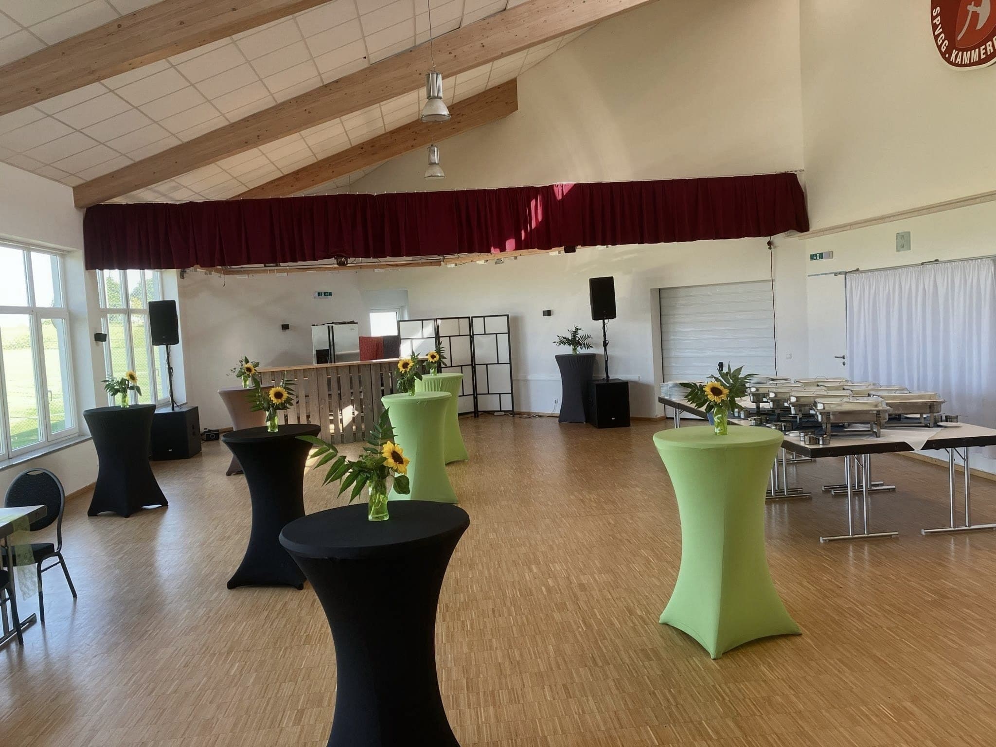 Event-Location Kammerberg mit Stehtischen, Sonnenblumen und Bordeaux-Vorhang vor dem Buffet